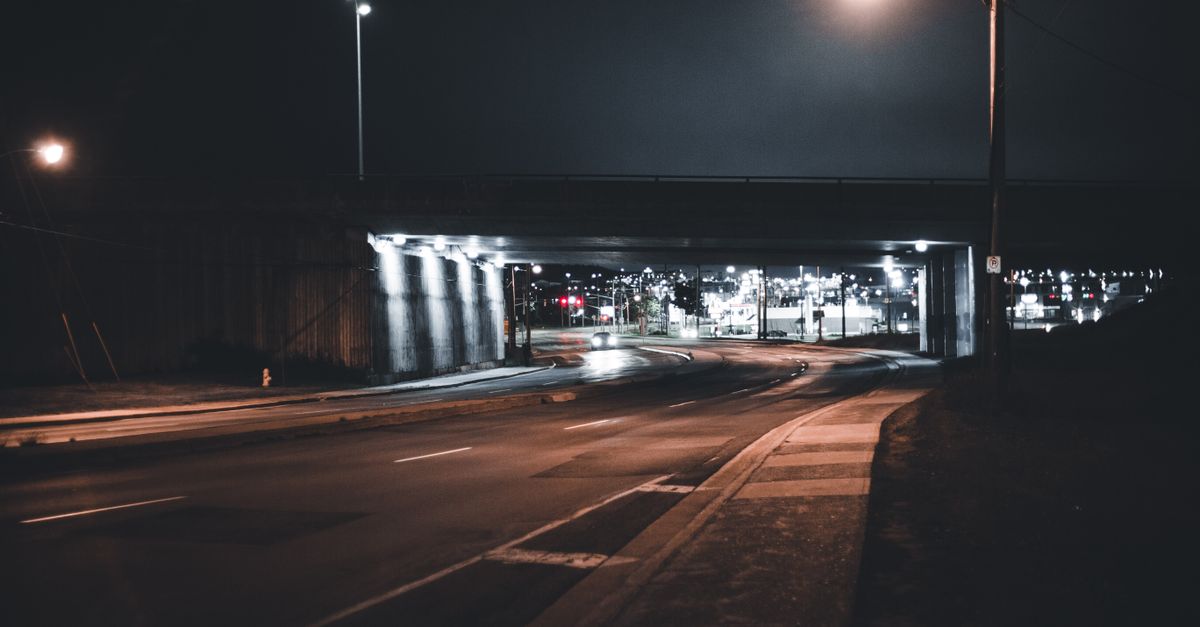Rue urbaine éclairée la nuit par des luminaires alignés le long du trottoir.
