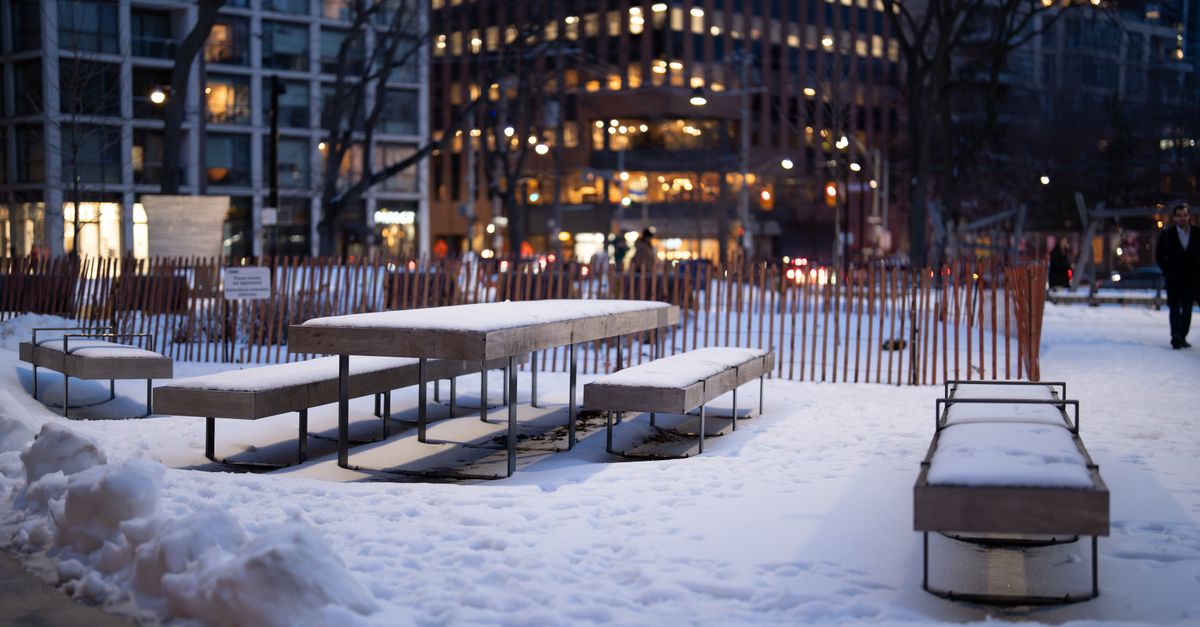 Banc public et poteau dans une rue enneigée sous un ciel d'hiver.